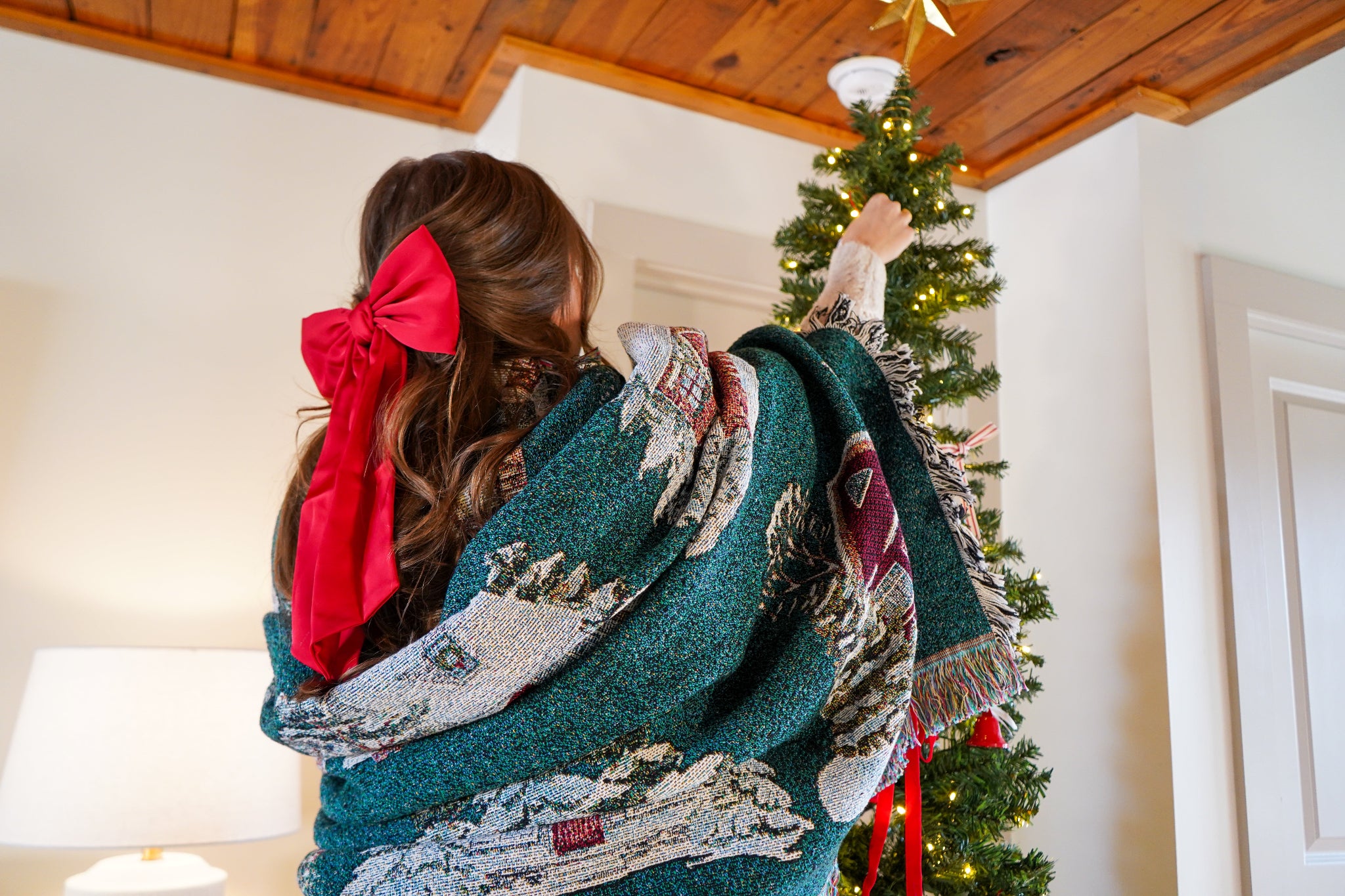 Woman decorating a Christmas tree with a patterned blanket draped over her shoulders.