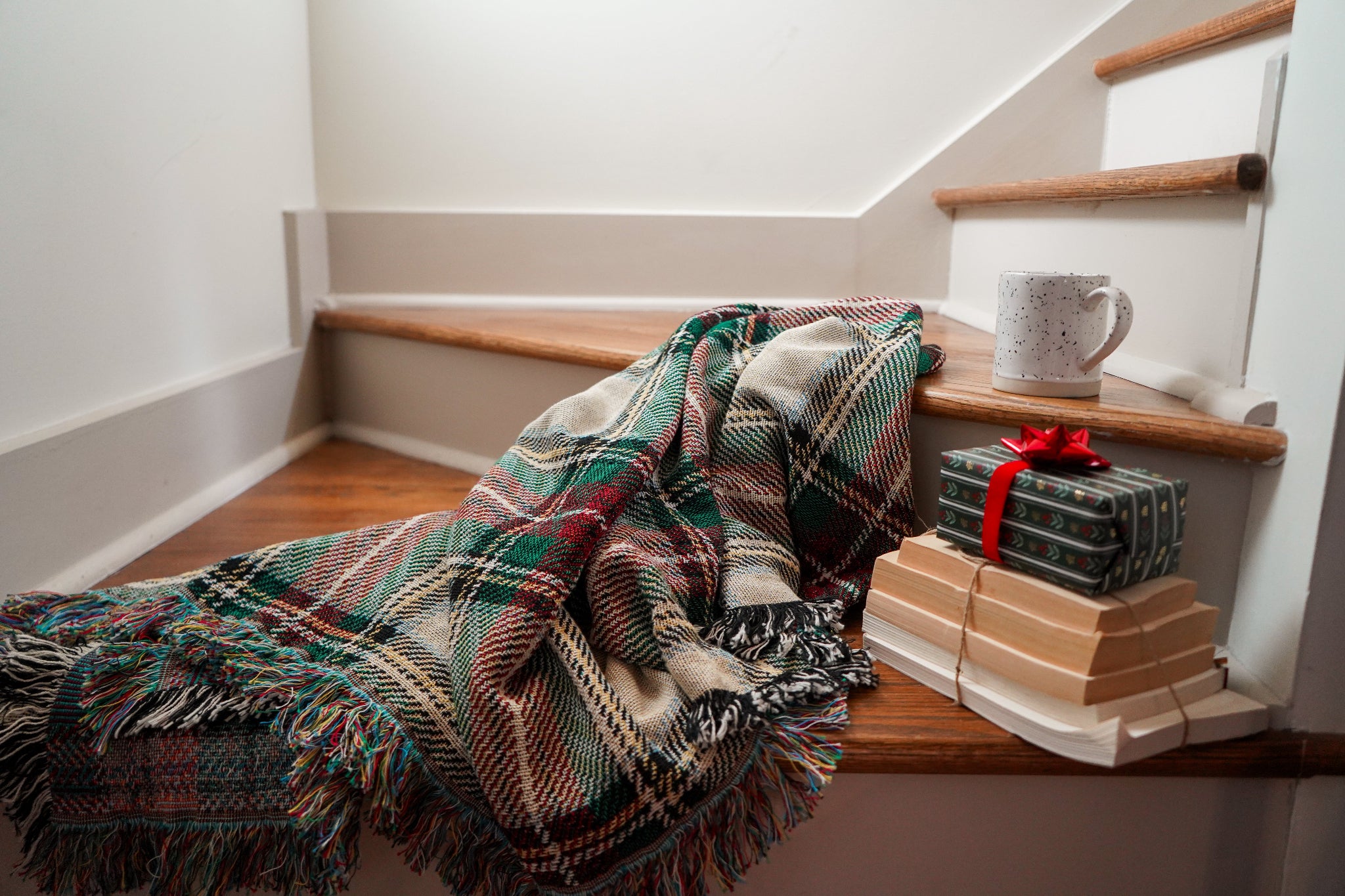 Plaid blanket draped over a staircase with wrapped gifts and a mug on the steps.