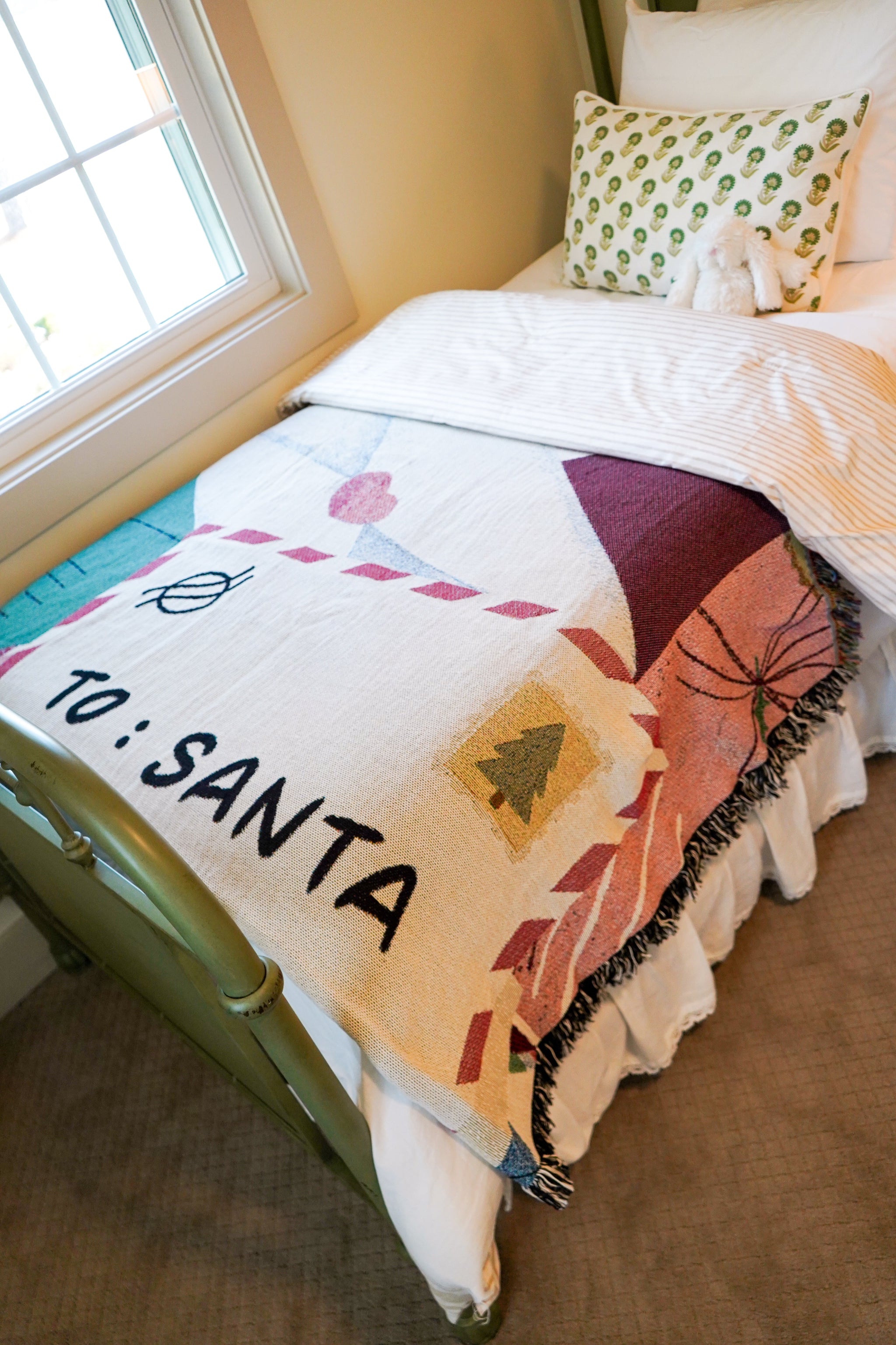 Bed with a colorful blanket labeled 'To: Santa' in a cozy bedroom setting.